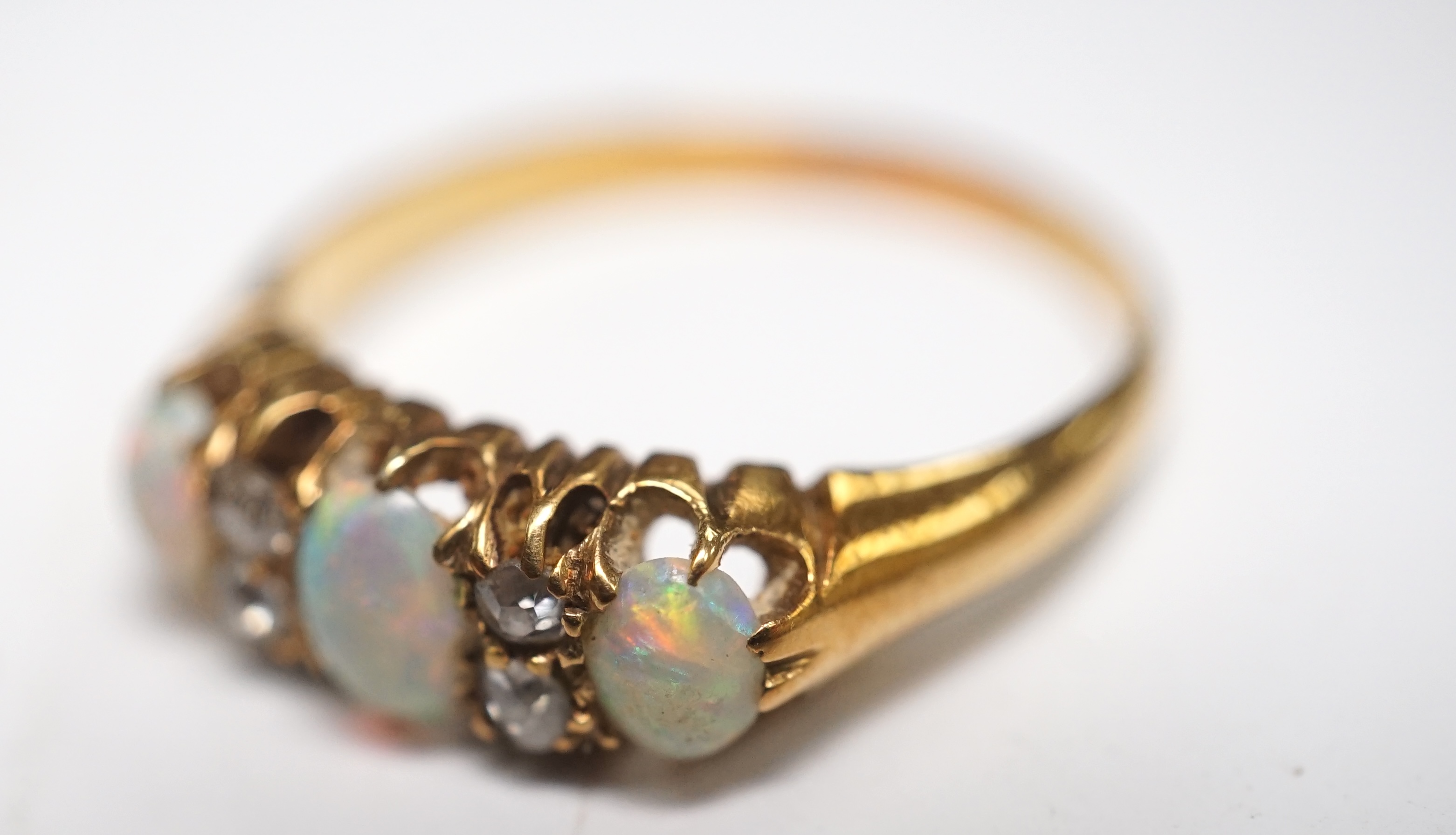 An early 20th century yellow metal and three stone white opal ring, with four stone diamond chip spacers, size M/N, gross weight 3 grams. Condition - poor to fair